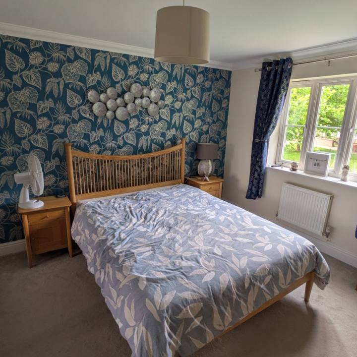 Bedroom before finishing, with oak furniture, teal wallpaper and patterned navy curtains.